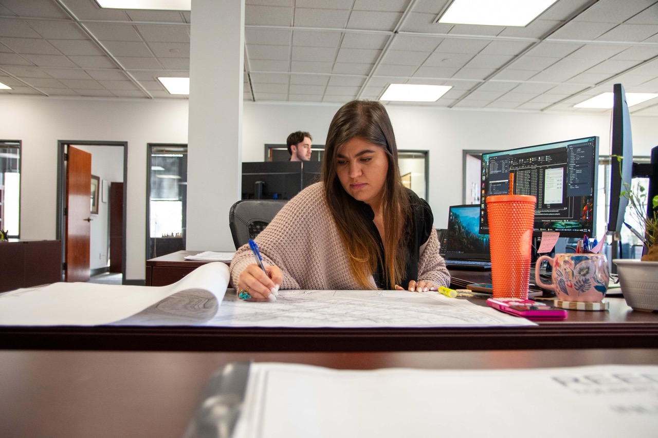 PEC employee focused on writing on large paper at her desk in an PEC Atlanta East office with computer monitors nearby.