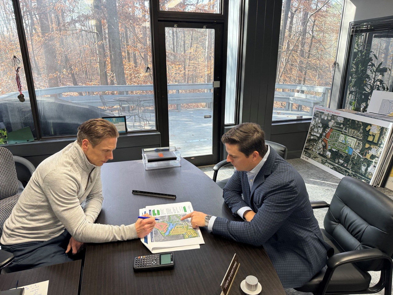 Two men seated at a conference table reviewing a site plan document, one pointing at it and the other holding a pen.