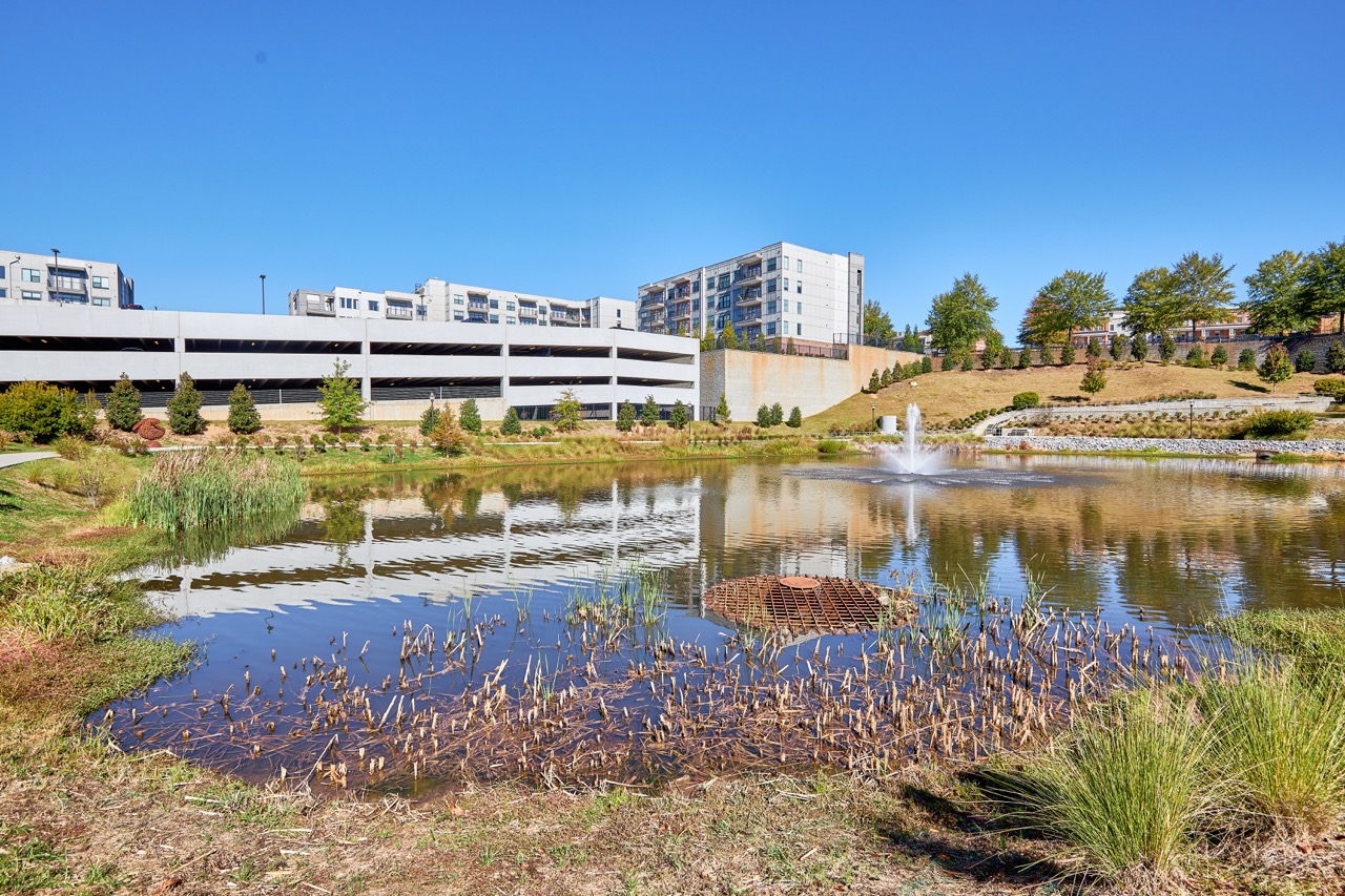 Wide view of the pond and fountain at Sienna Apartments with surrounding residential buildings.