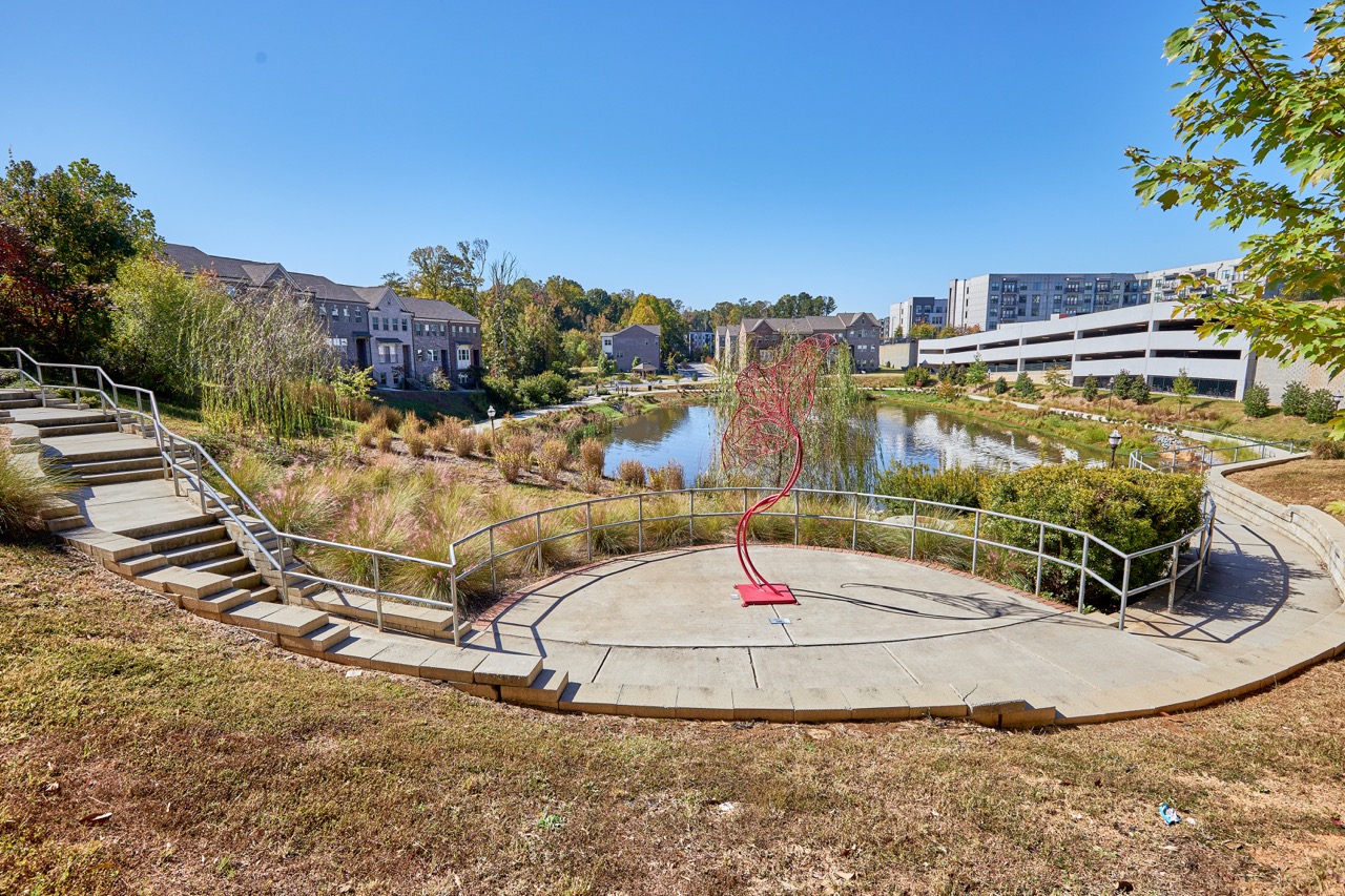 Outdoor gathering area at Sienna Apartments overlooking a pond, featuring a red abstract sculpture.