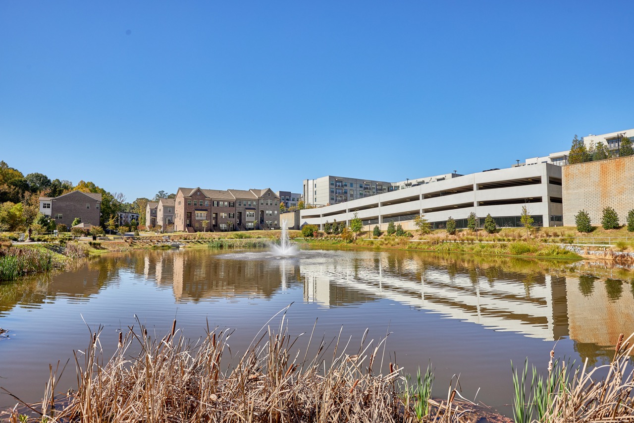 Pond and water fountain at Sienna Apartments with parking deck and residential buildings in the background.