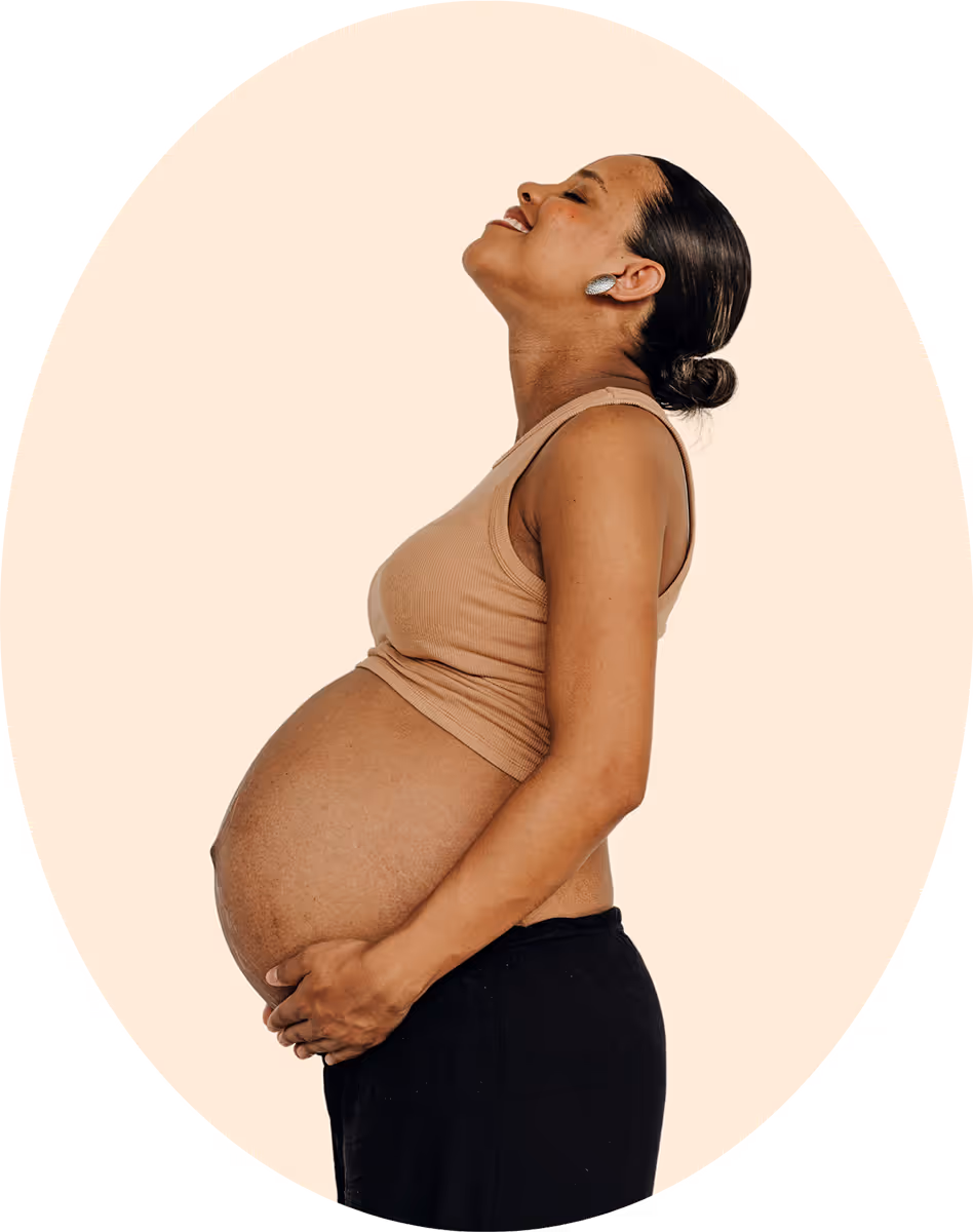 Pregnant woman smiling and looking up while cradling her belly.
