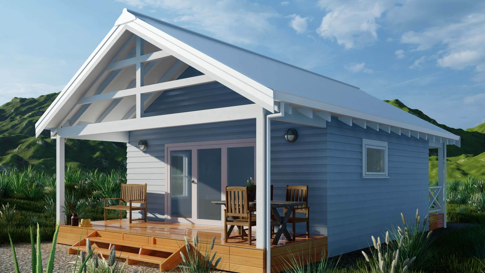 Small blue cottage with white trim and a covered wooden porch featuring chairs and a table, surrounded by grass and hills.