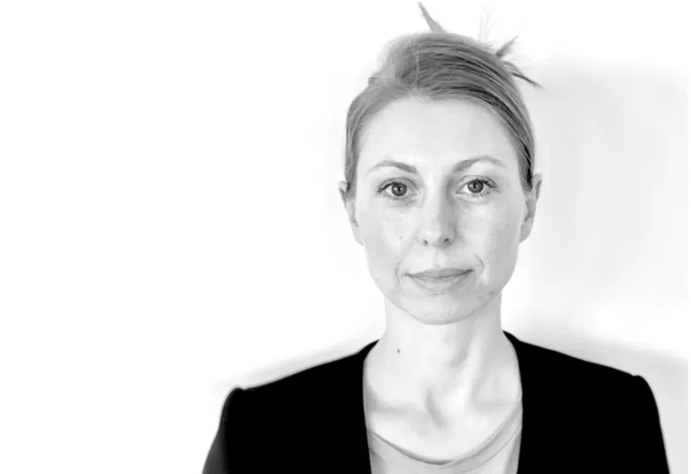 Black and white headshot of a woman with light skin and hair pulled back, wearing a dark blazer over a light top.
