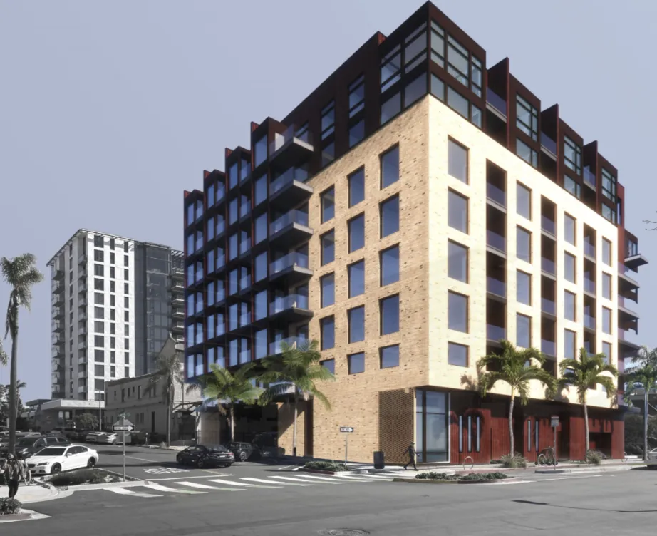 Modern multi-story apartment building with light brick facade and dark upper sections, palm trees lining the street corner.