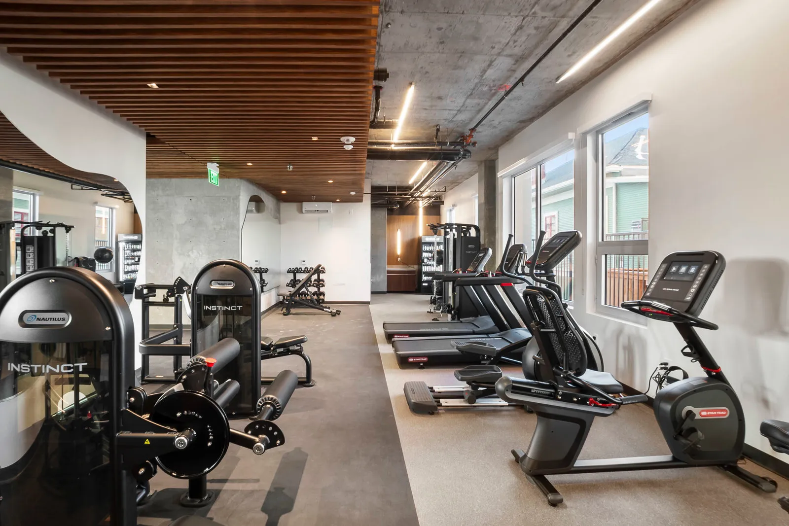 Modern gym room with weight machines, treadmills, exercise bikes, and large windows.
