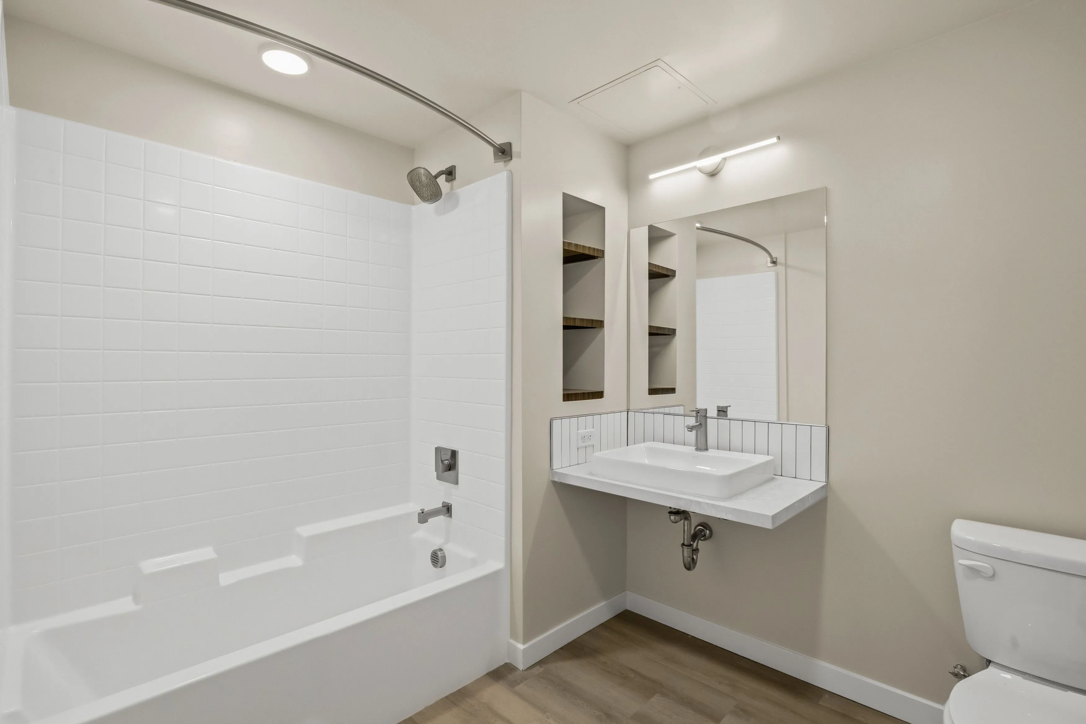 Clean bathroom with white bathtub, showerhead, wall tiles, floating sink, mirror, and toilet.