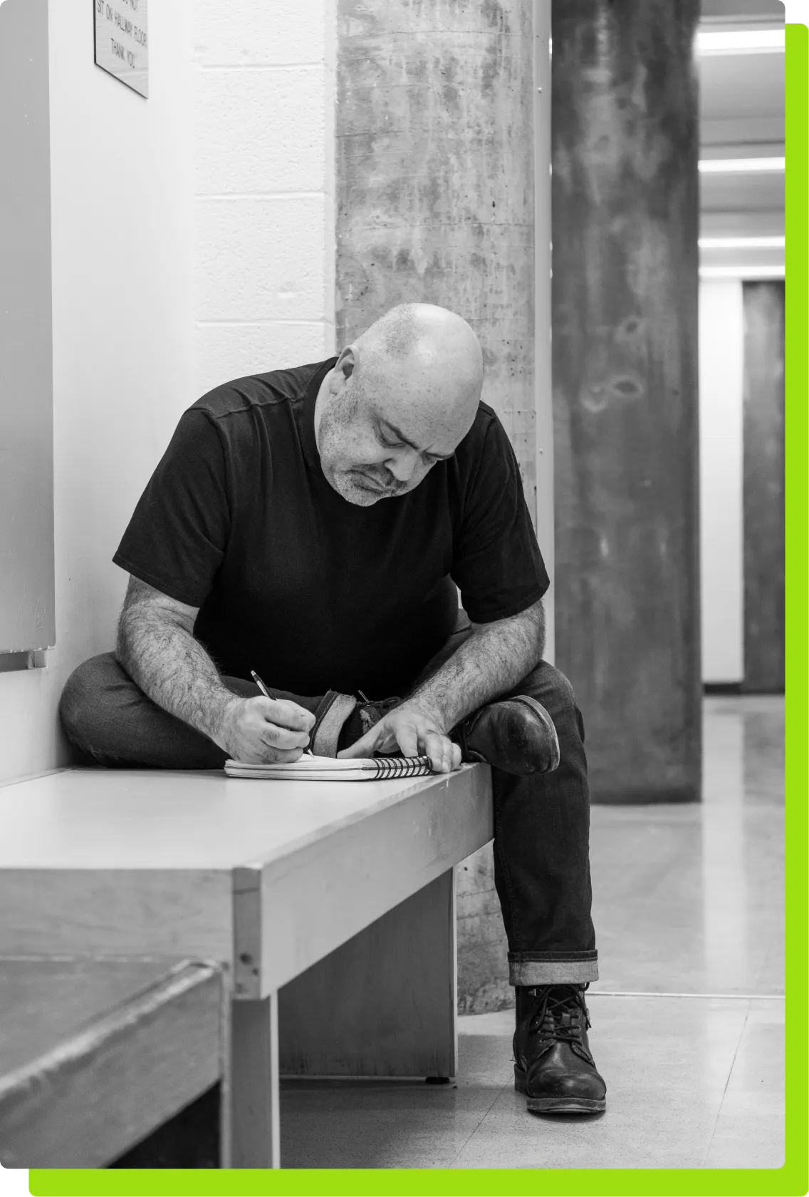 A black and white photo of Robert Smith writing notes on a wooden bench.