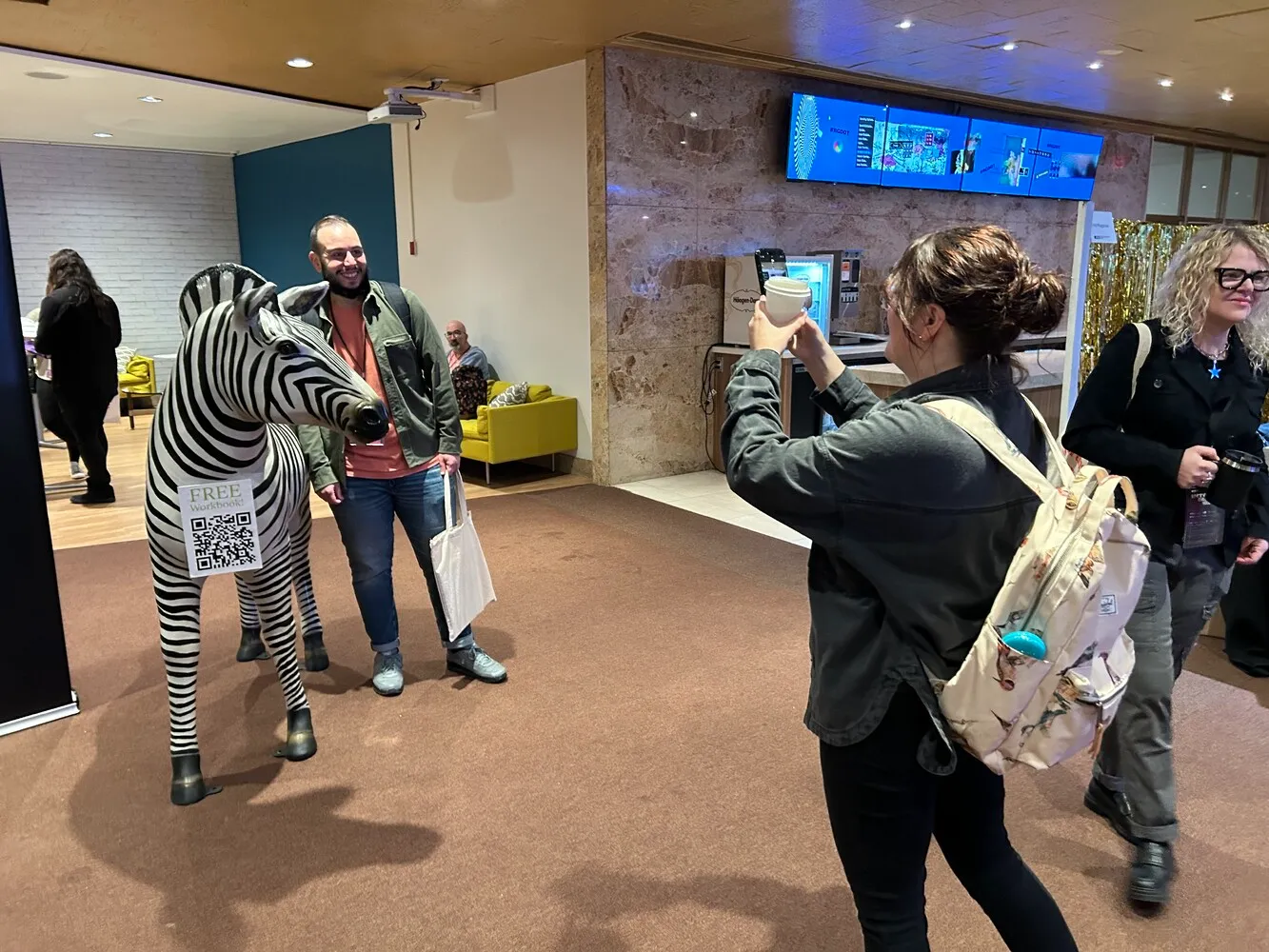 A man posing with the 5-foot zebra status while woman takes a photo