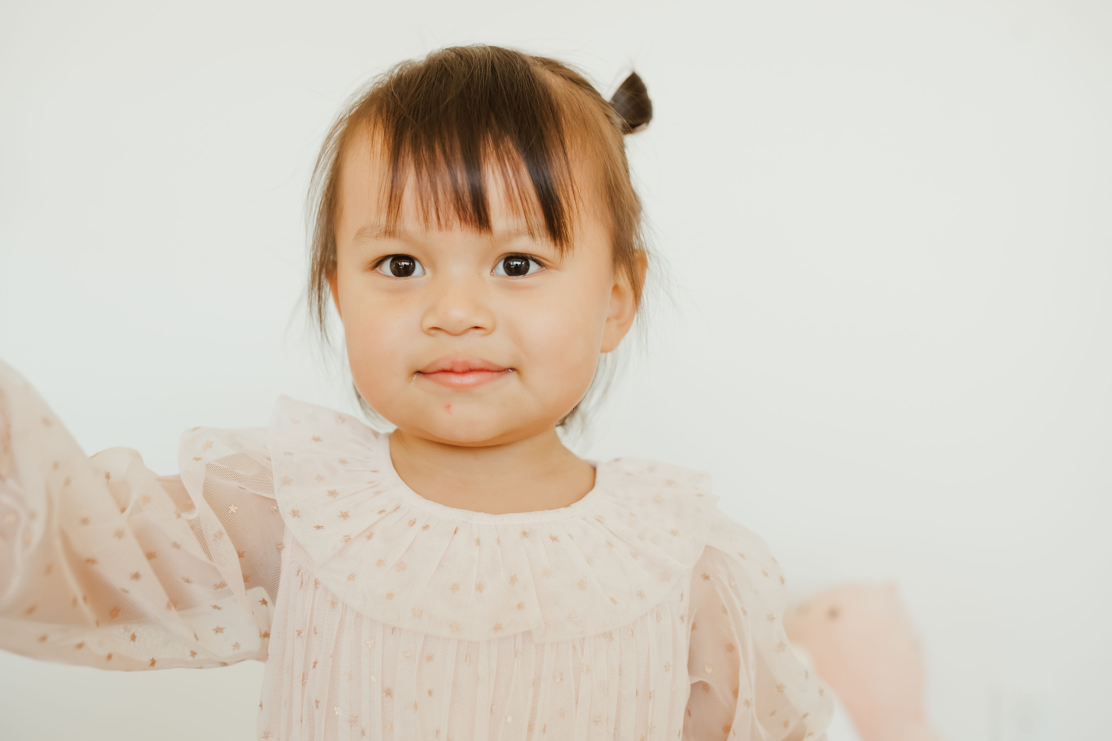 A smiling woman in purple scrubs sitting on a rug with seven young children in a playroom with wooden educational boards on the wall.