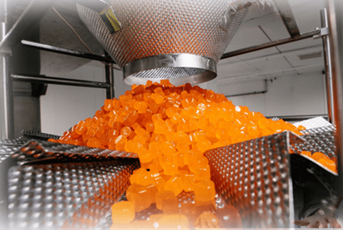 Gummy producing machine outputting a large quantity of orange colored gummies