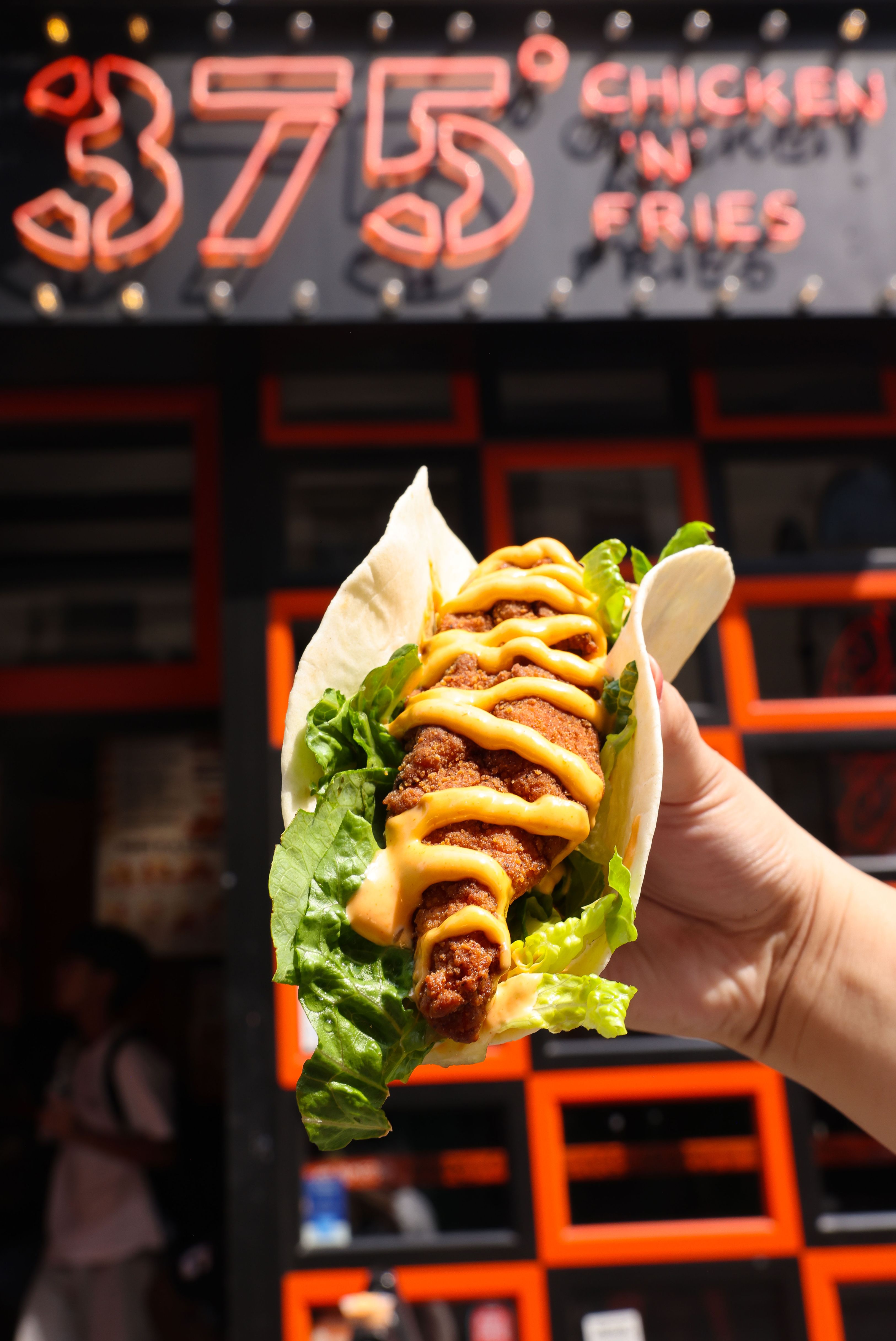 Man wearing glasses and a pink shirt eating a sandwich outdoors.