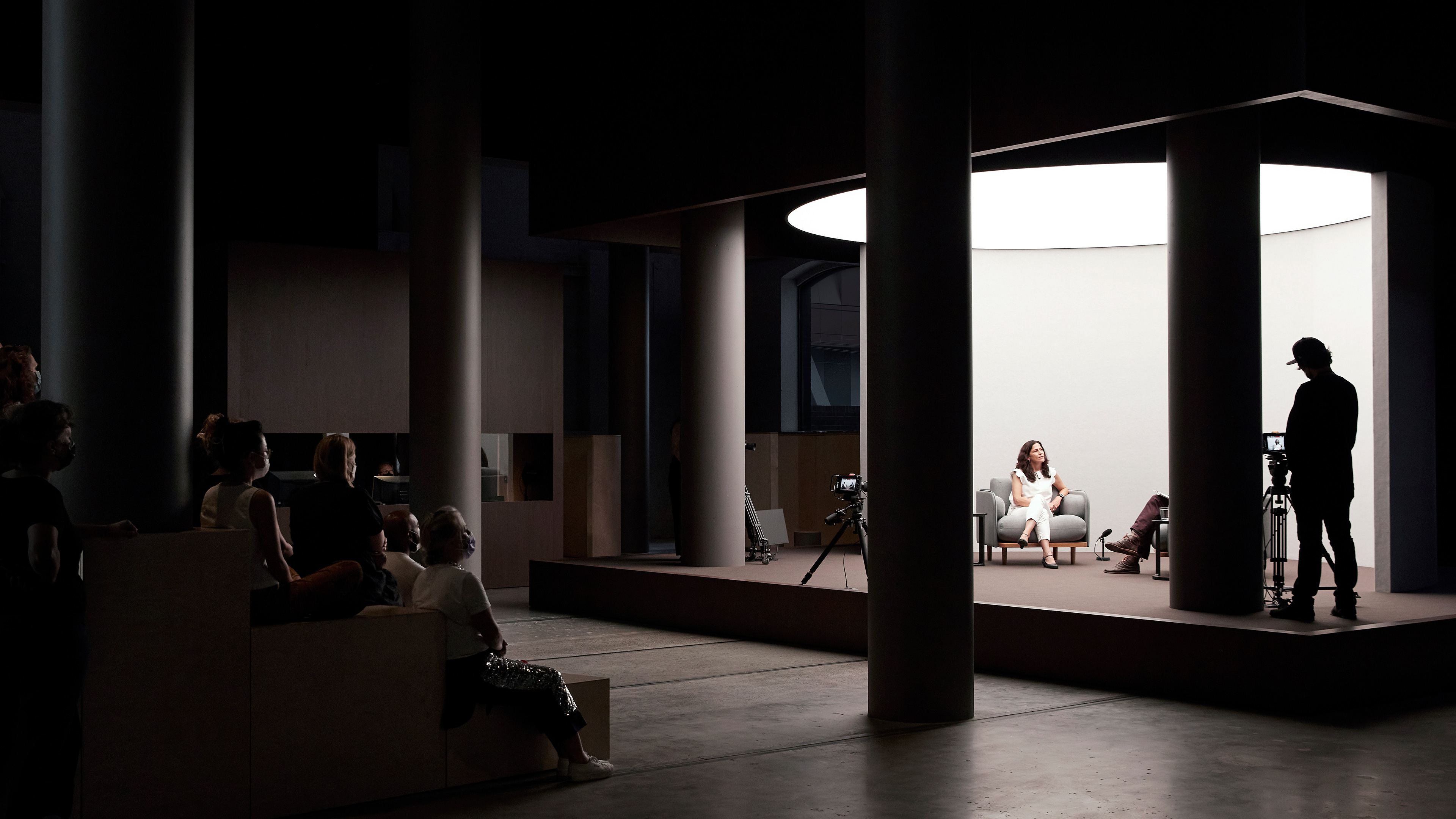 Woman interviewed on a well-lit stage in front of a small audience.