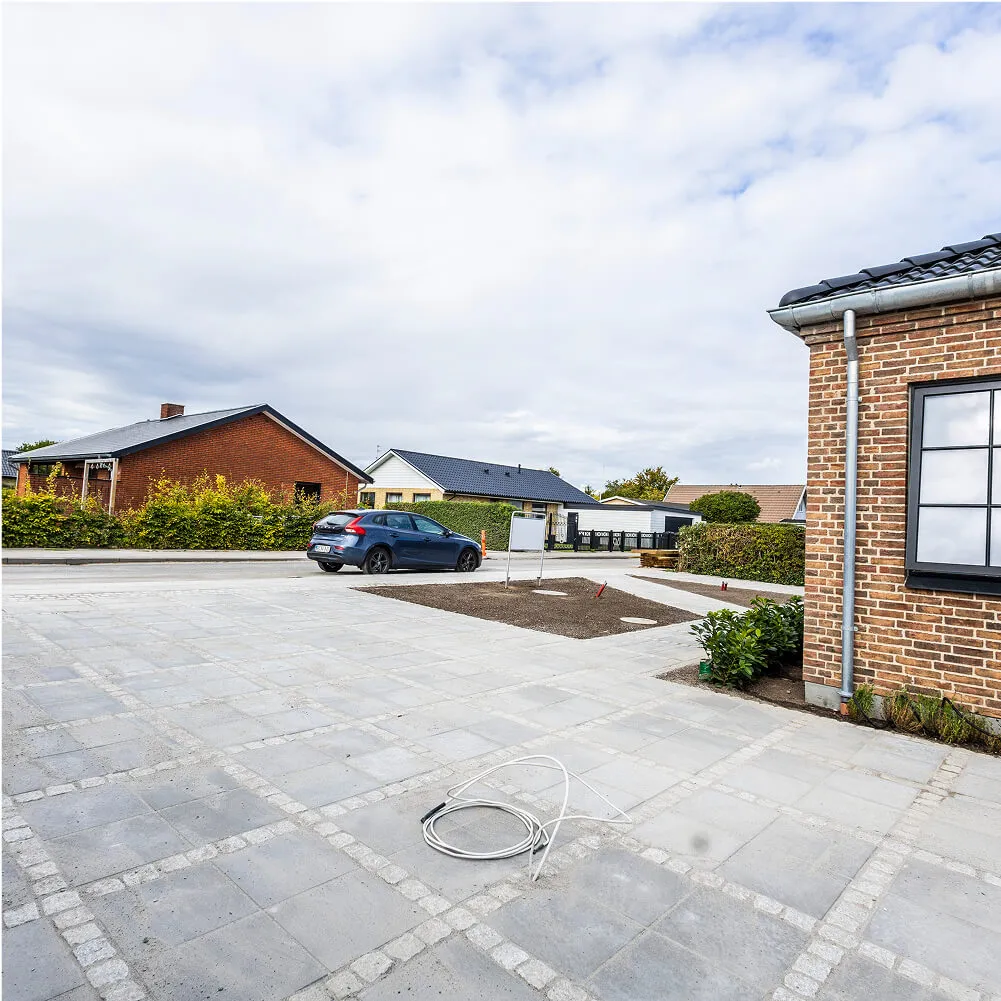 Stort fliseareal i rådhusbelægning, set mod vej og indkørsel.