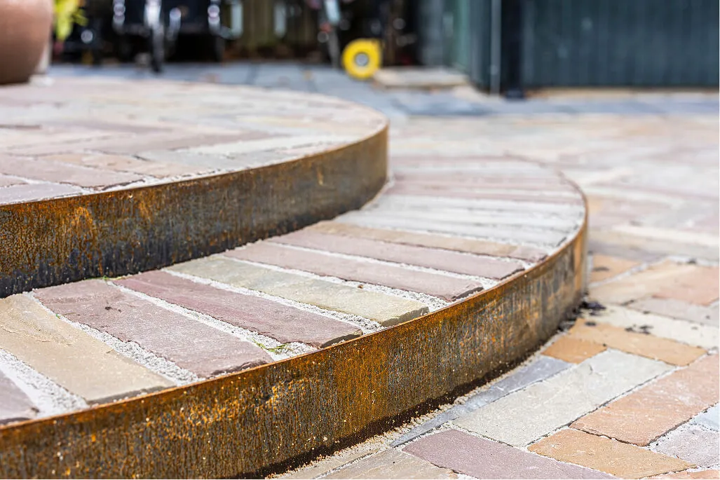 Trapperin dækket med belægningssten, hvor kanten er markeret med cortenstål