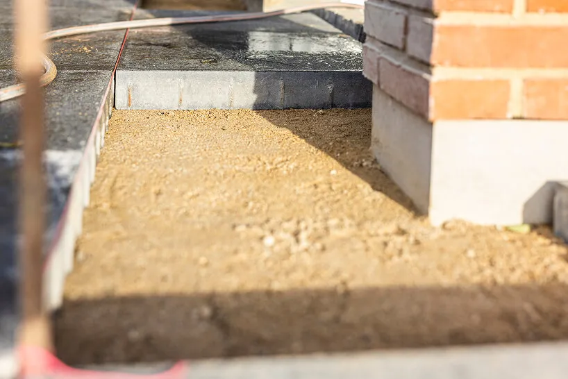 Opgravet jordområde ved siden af murstensbygning og nydelig sortsti i byggeplads.