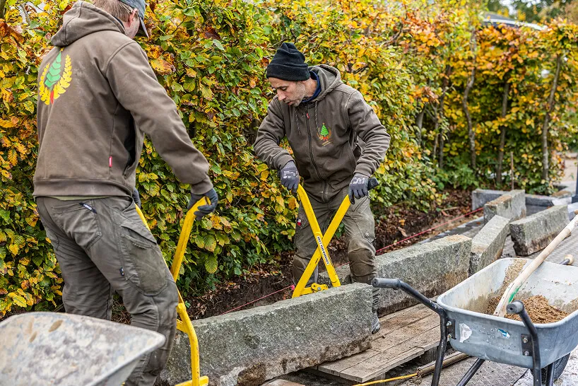 To mænd med arbejdstøj flytter en stor graniteblok ved hjælp af værktøj