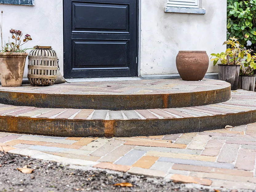 Halvrund trappe i natursten foran en sort dør, der skaber en flot kontrast til de lyse sten.