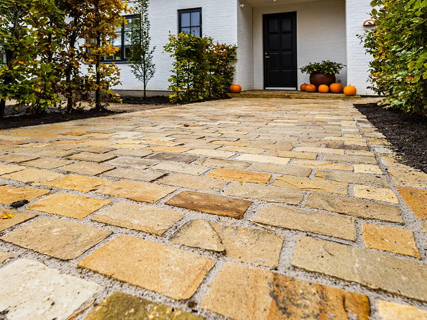 Nærbillede af brolægning i natursten lagt i et præcist mønster med fokus på de gyldne nuancer.