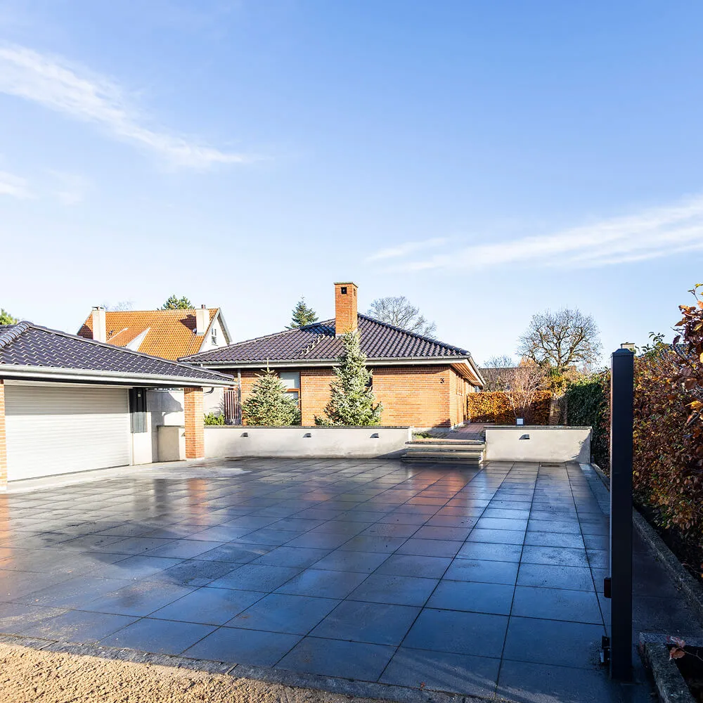 Finish i brolægning ved hvid garageport og muret trappeopgang.