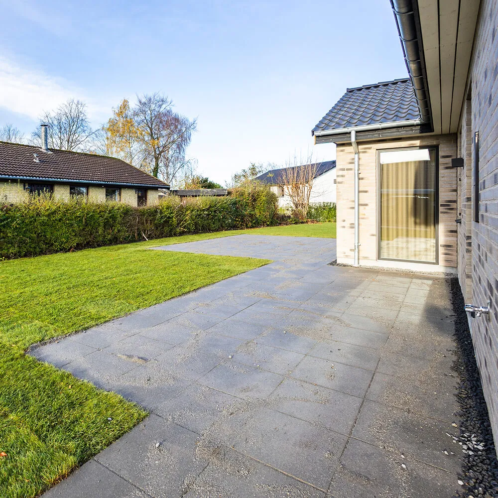 Sorte granitskærver lagt som præcis afslutning mod husets murværk.