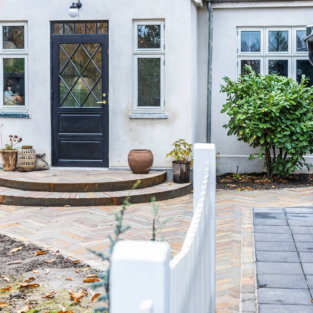 Oversigt over husets indgang med rundmuret trappe og dekorativ belægning.