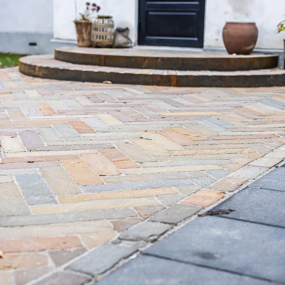 Indgang til hus med rundet trapp og flisebelagt fortov i forskellige pastelfarver.