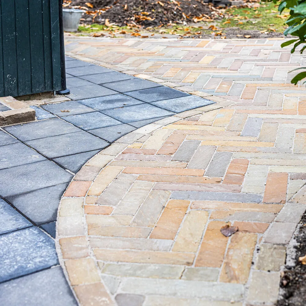 Præcis overgang fra mønstret natursten til mørkegrå betonfliser.