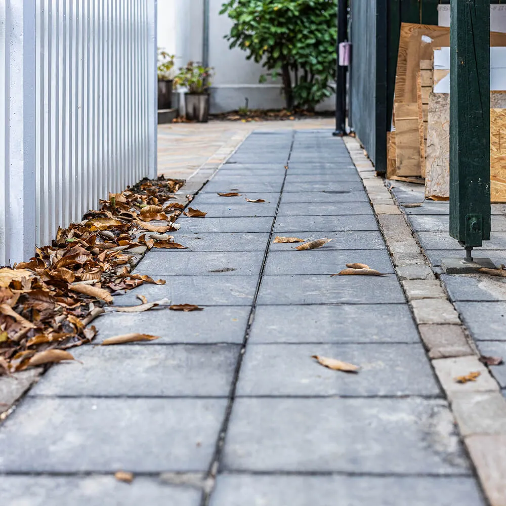 Klassisk gangsti med store grå betonfliser lagt præcist langs facaden.