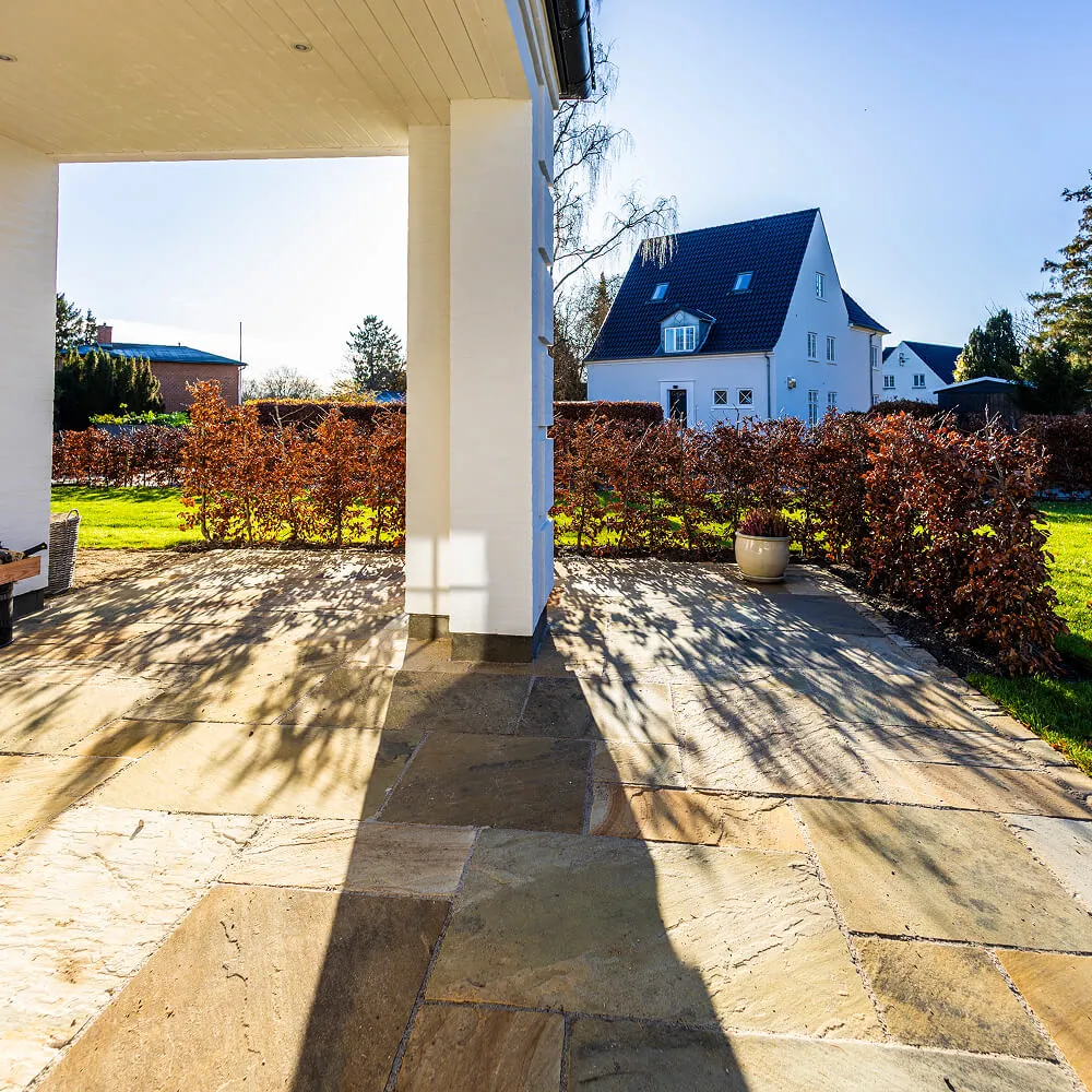 Terrasseareal under tag udført med store sandstensfliser i varme nuancer.