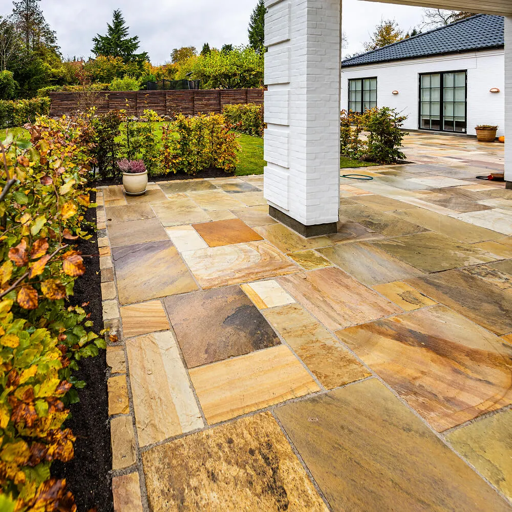 Detalje af præcis brolægning med natursten langs husets facade og bede.