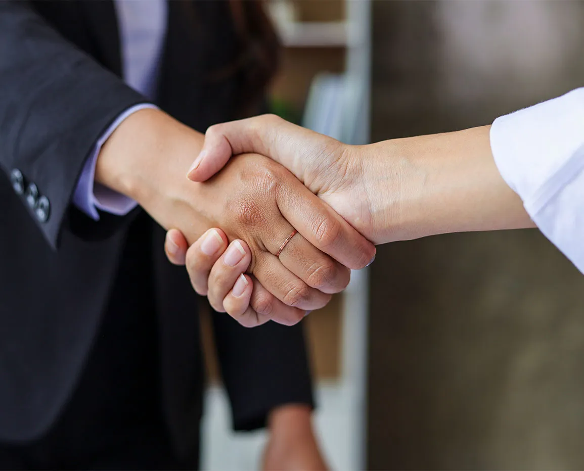 Close-up of two people shaking hands, one wearing a black suit and the other a white shirt.