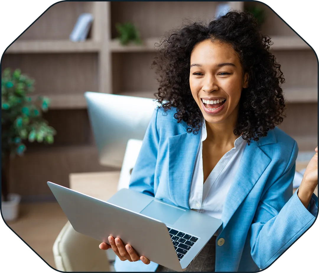 Smiling woman in blue blazer holding a laptop in a modern office setting.