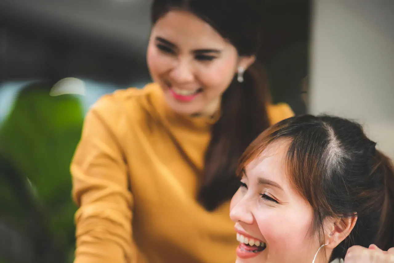 Two women smiling and enjoying a moment together, one wearing orange and the other with hoop earrings.