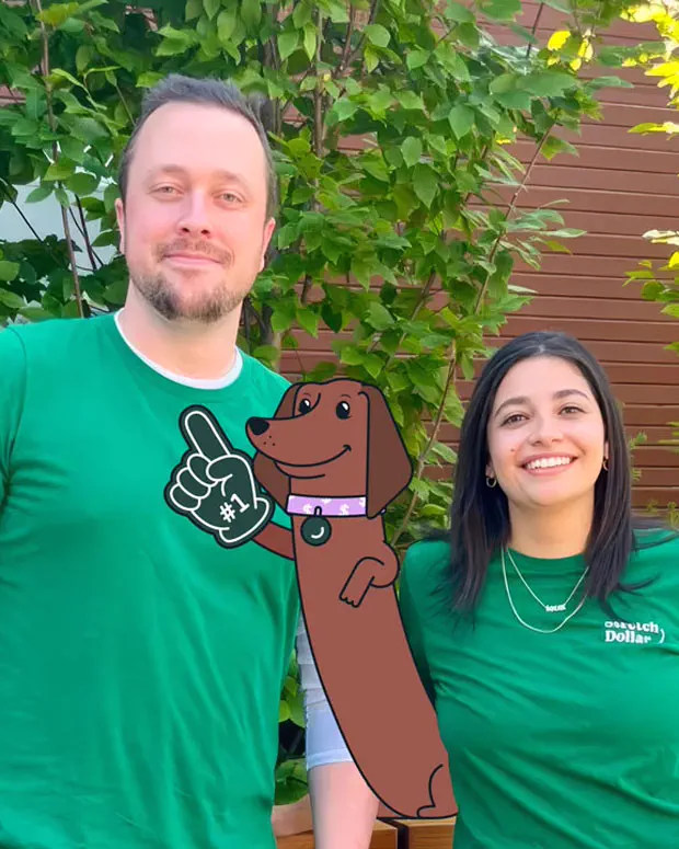 The co-founders of StretchDollar, Marshall and Kaiza, stand outdoors with a cartoon brown dog wearing a foam finger.