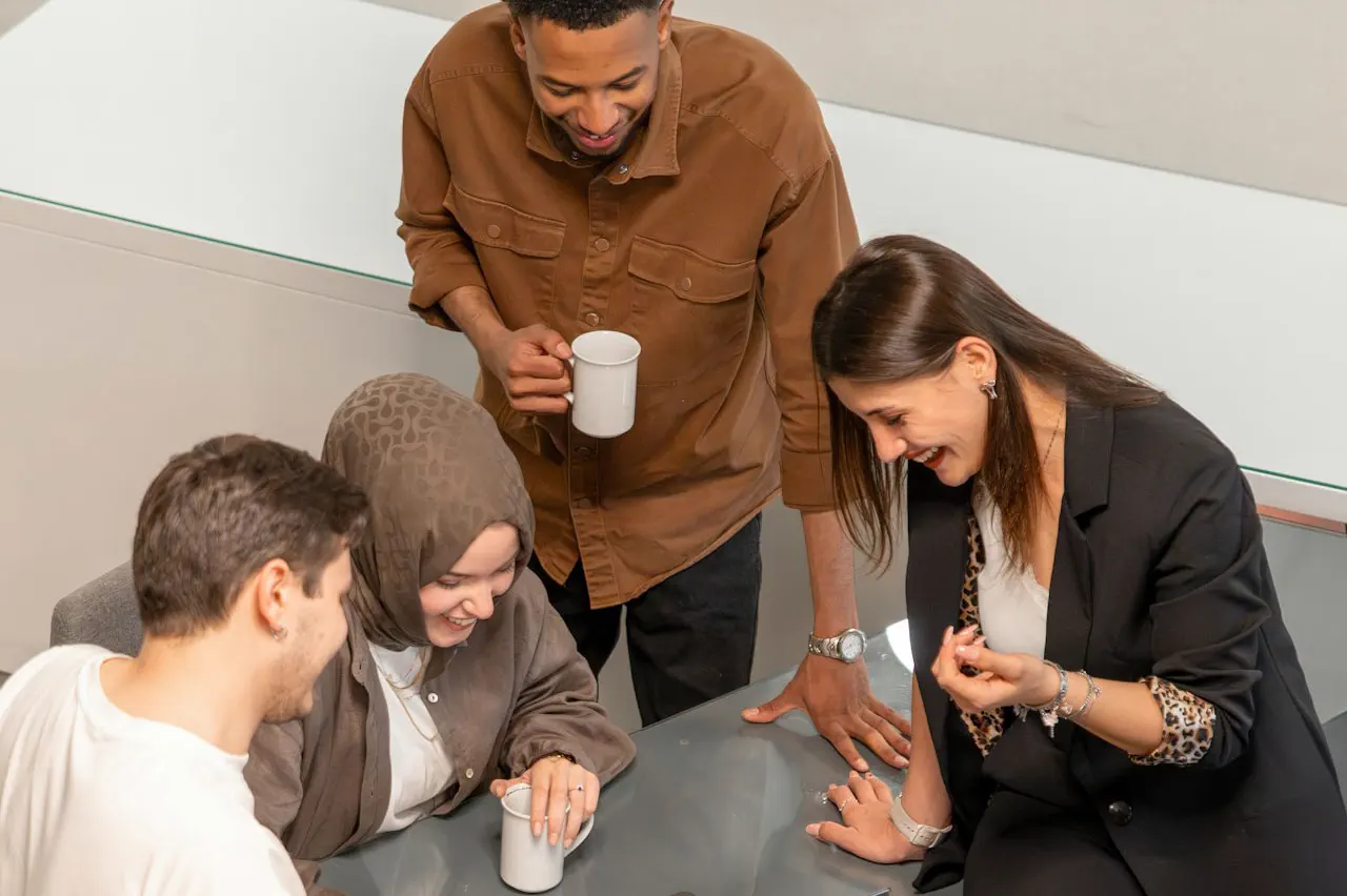 Four young adults laughing and chatting around a glass table.