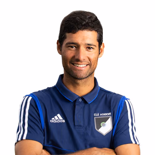 Smiling man with short dark hair wearing a blue Adidas polo shirt with Ellé Academy logo, arms crossed.