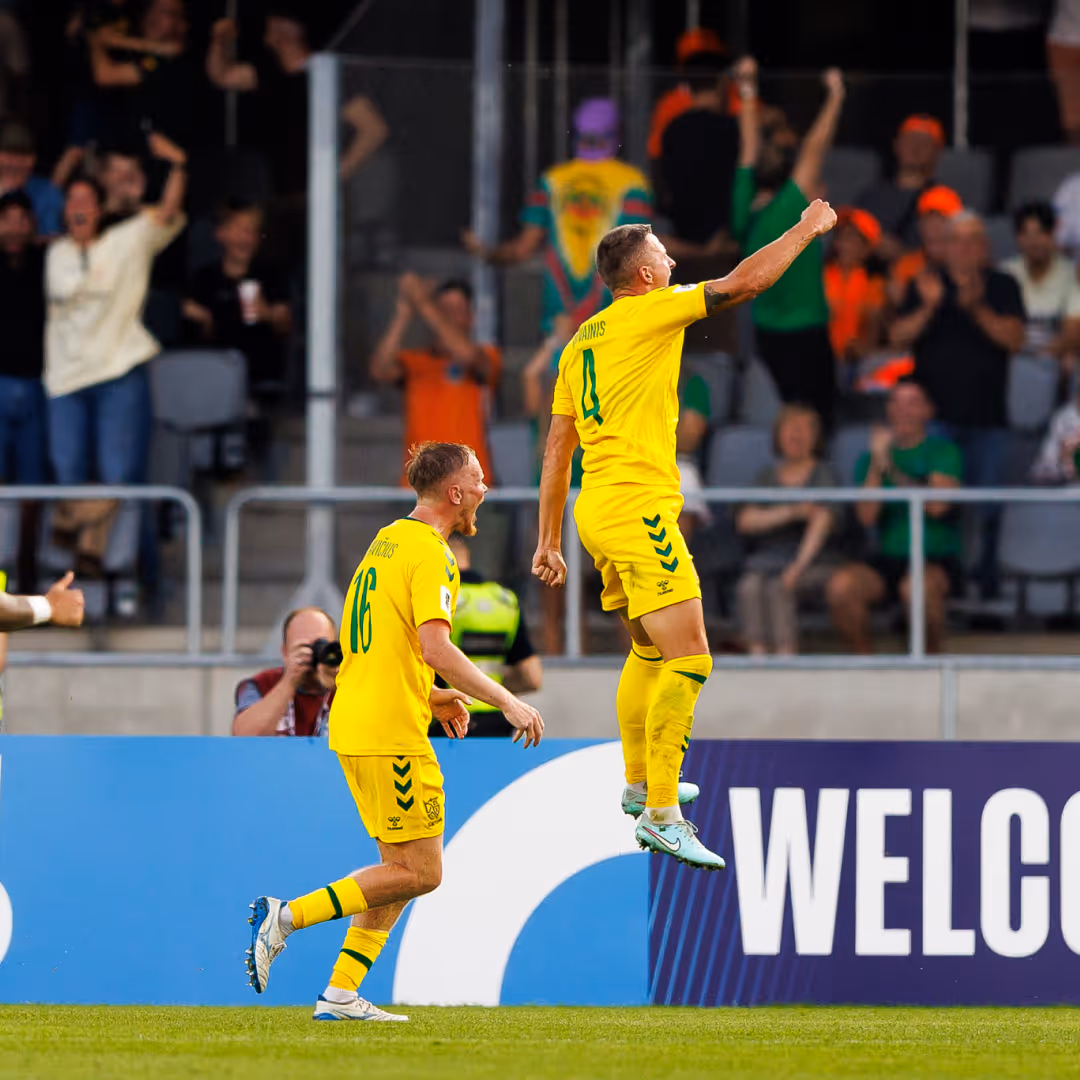Two soccer players in yellow uniforms celebrating a goal with one player jumping and raising his fist.