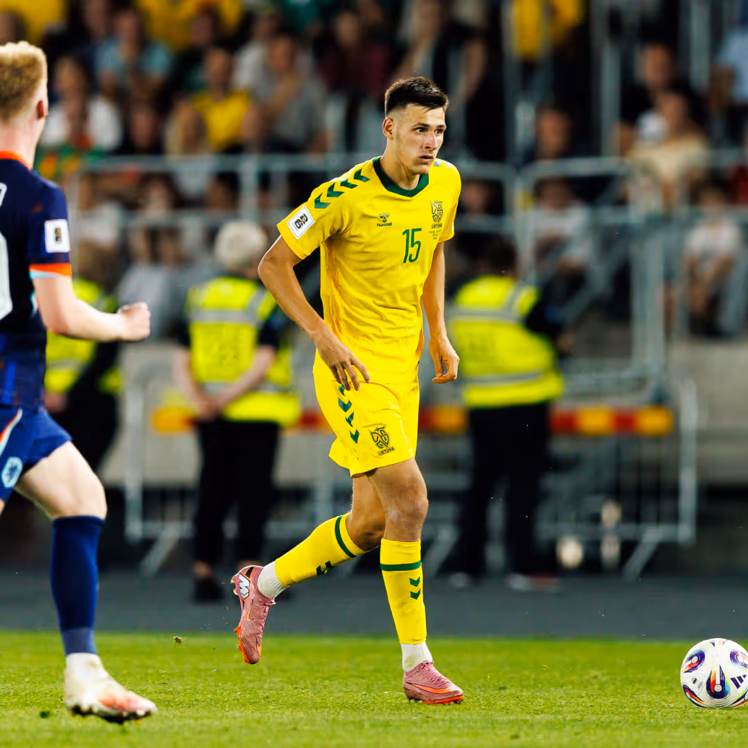 Soccer player in yellow uniform with number 15 running on field during match, with opponent and crowd in background.