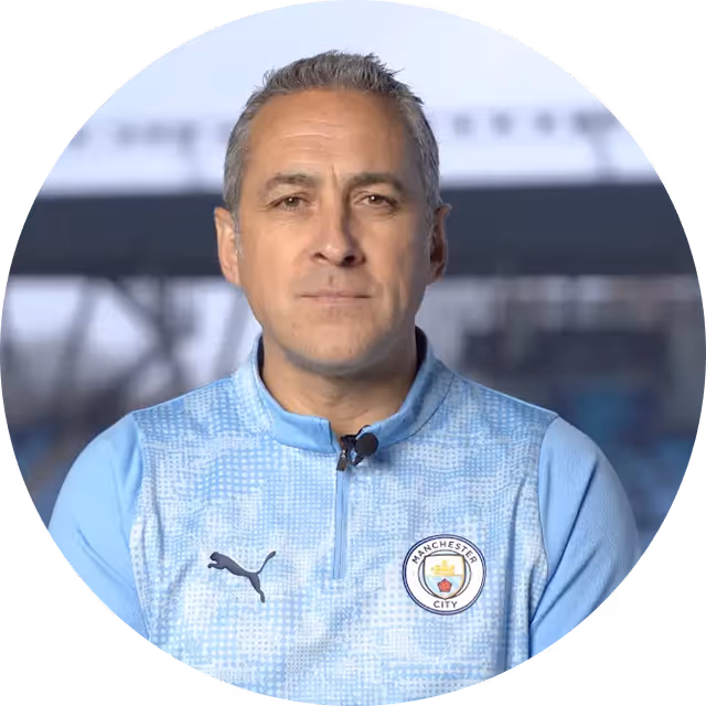Man wearing light blue Manchester City Puma sports jacket looking directly at the camera with a blurred outdoor background.