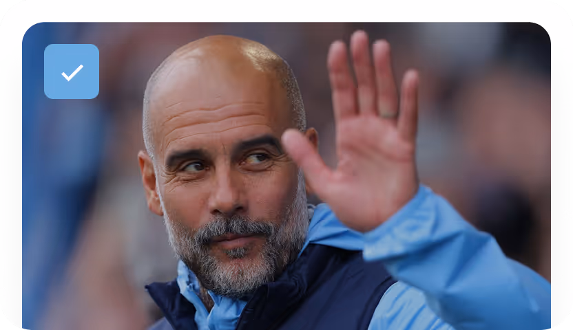 Man with a bald head and beard waving his hand while wearing a blue jacket with a hood.