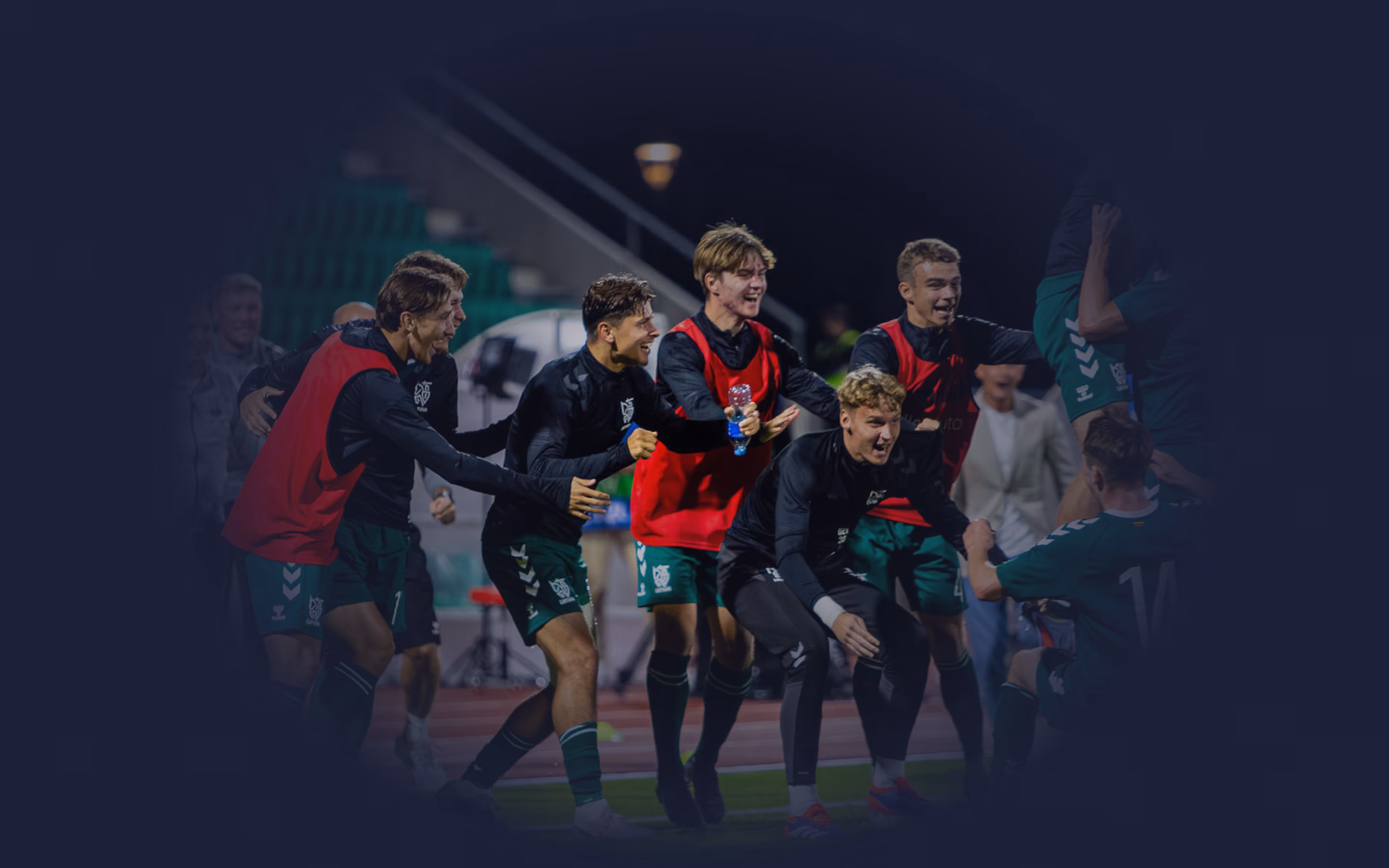 Fußballspieler in Trainingsleibchen jubeln gemeinsam an der Seitenlinie