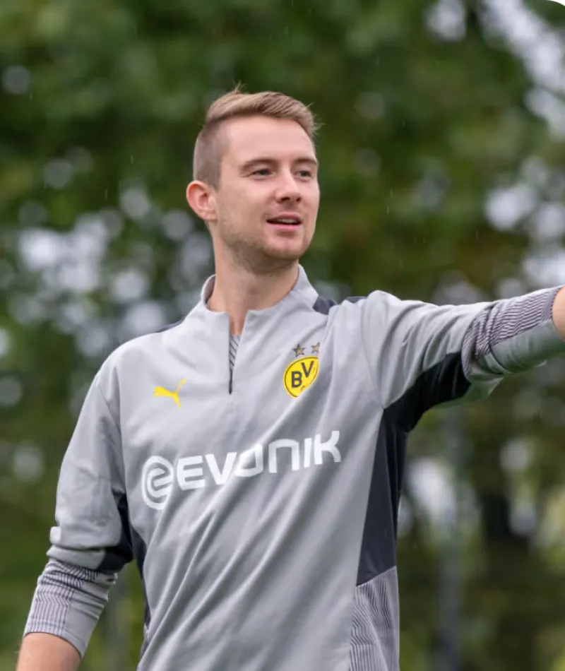 Coach in a grey Borussia Dortmund training top pointing and giving instructions outdoors