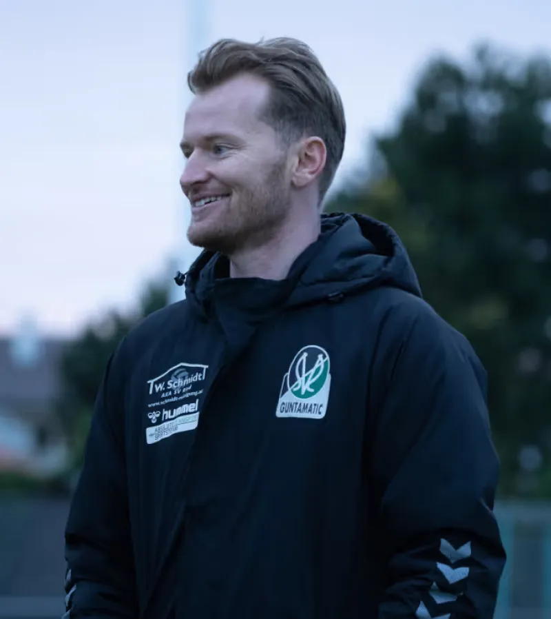 Smiling coach in a dark training jacket standing on a football pitch