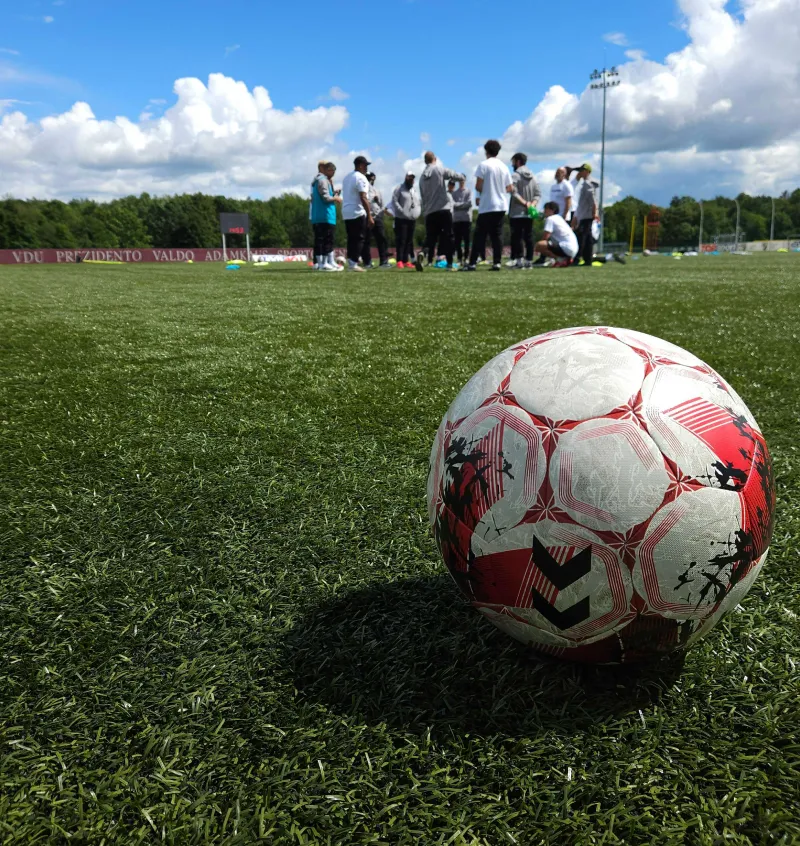 Football on a grass pitch with a group of players gathered in the background