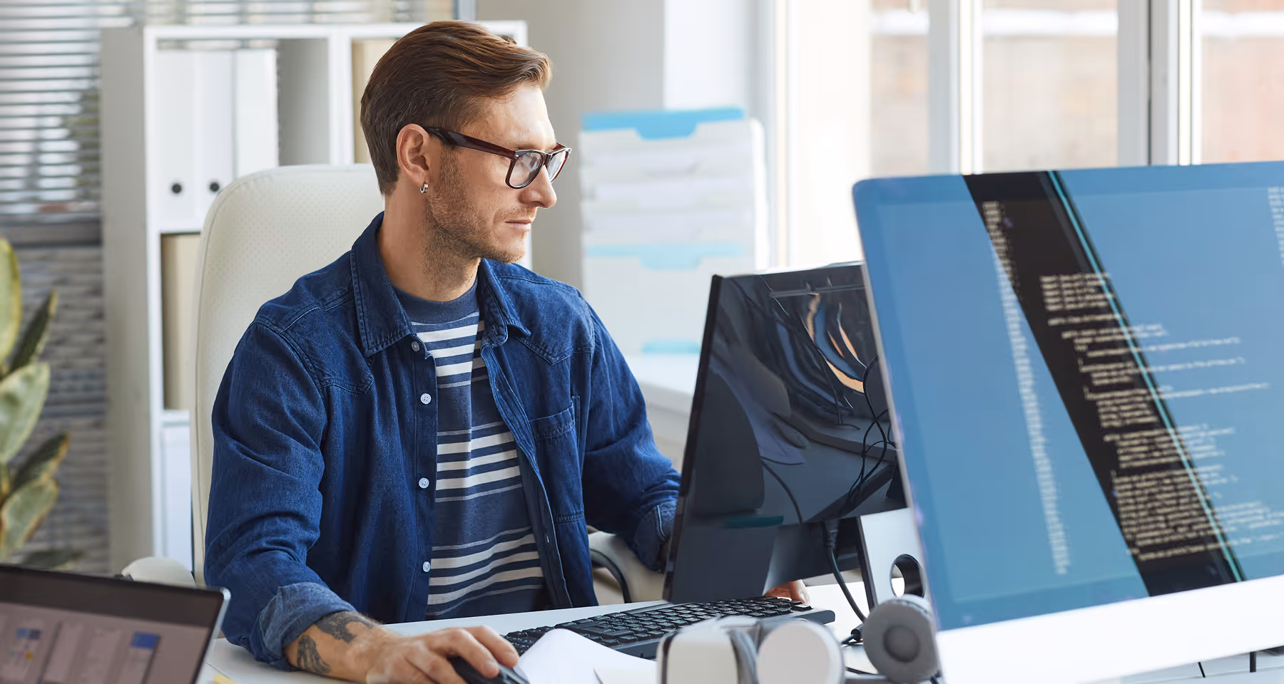 Man with glasses working on a desktop computer in a bright office environment.