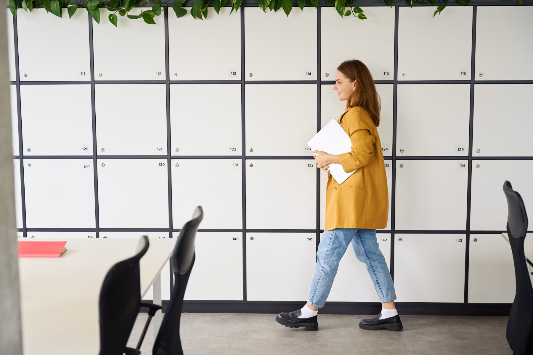 Woman in a white coat standing in a parking garage holding car keys, folders, and a black bag, looking towards a black car.