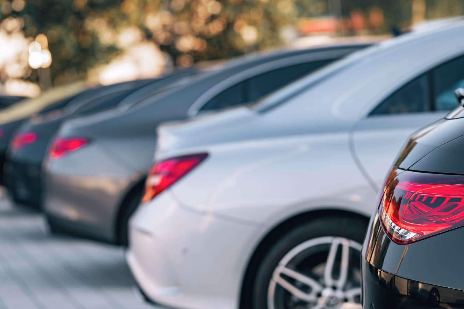 Woman in a white coat standing in a parking garage holding car keys, folders, and a black bag, looking towards a black car.