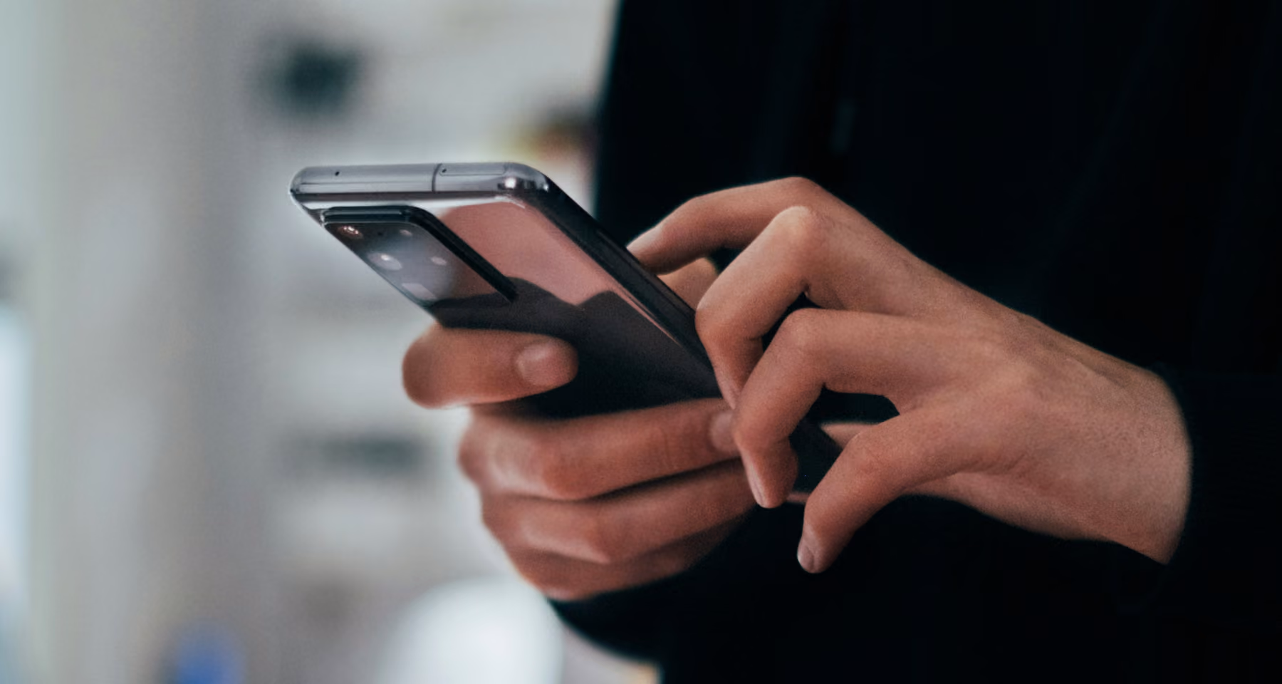 Una persona con indosso una maglia nera che tiene e utilizza uno smartphone moderno con una fotocamera posteriore multipla.