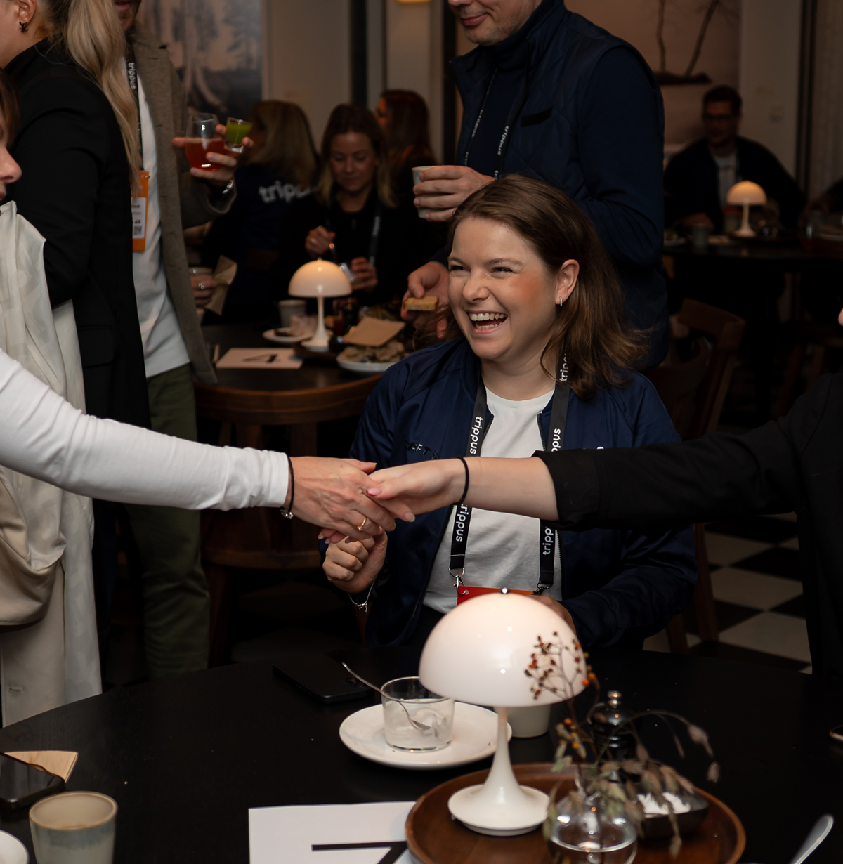 En person som skrattar när två andra personer skakar hand på ett event.